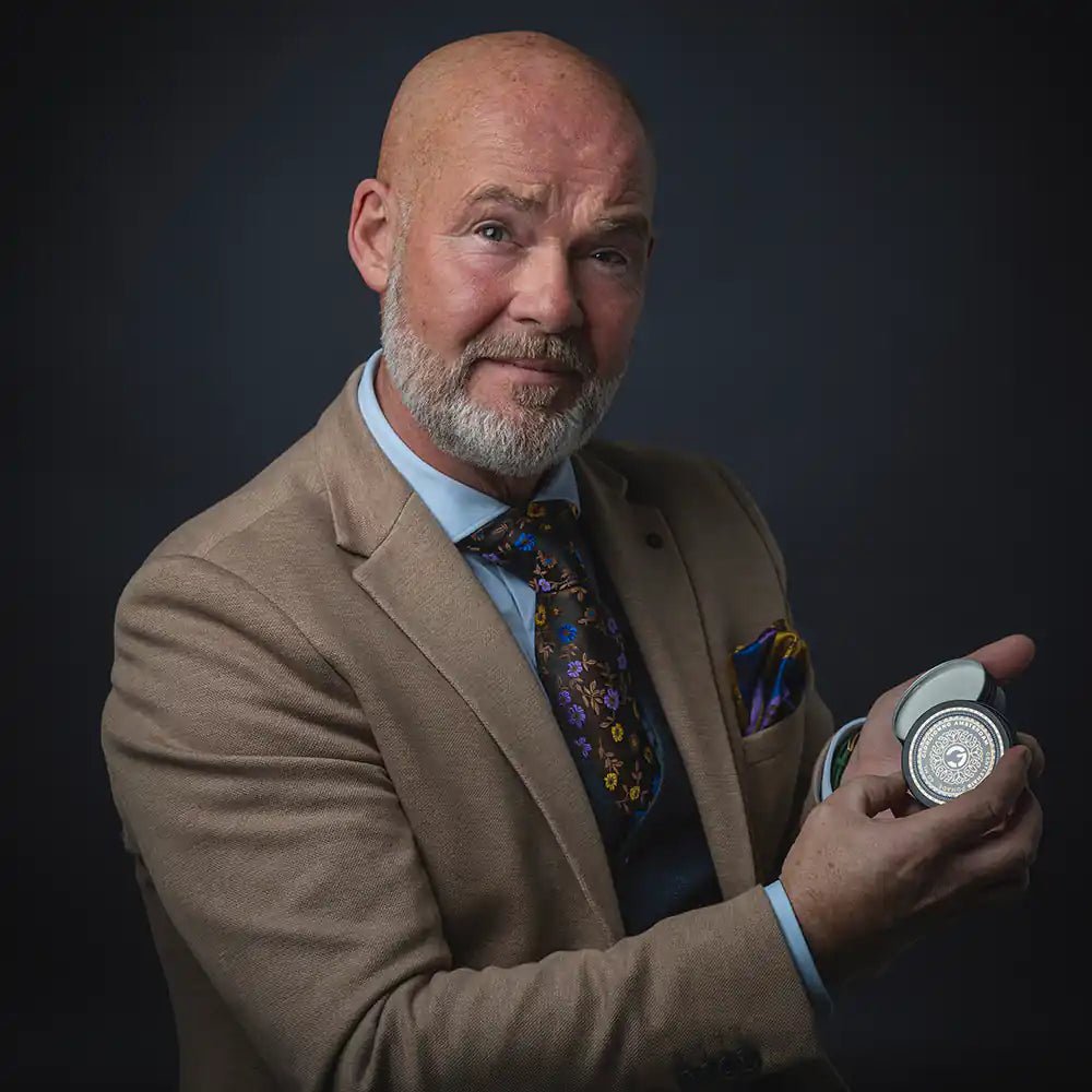 Zakelijke man met baard en colbert toont een luxe verzorgingscontainer tegen een donkere achtergrond.