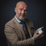 Zakelijke man met baard en colbert toont een luxe verzorgingscontainer tegen een donkere achtergrond.