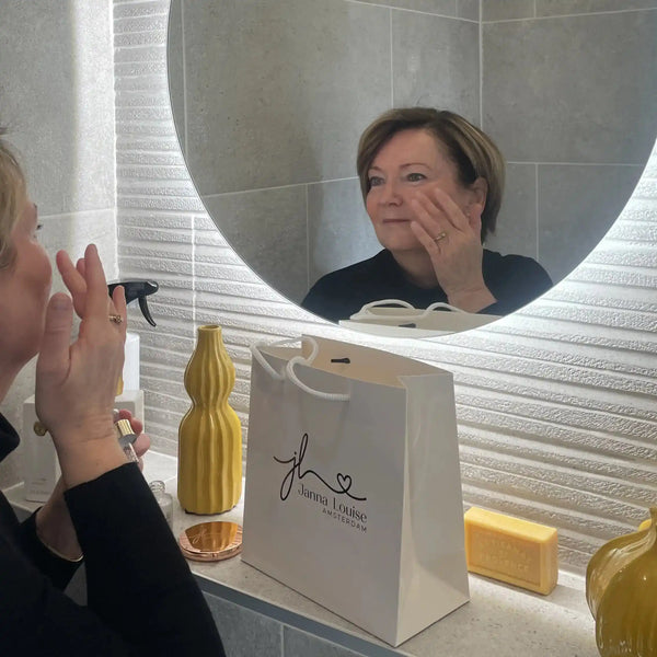 Vrouw brengt gezichtsverzorging aan voor een verlichte spiegel in een moderne badkamer met luxe uitstraling.