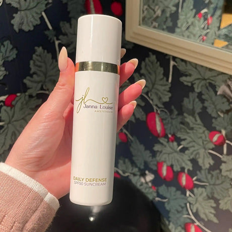 Hand houdt flesje Janna Louise Amsterdam Daily Defense SPF50 zonbescherming tegen achtergrond met groene bladeren en rode bessen.