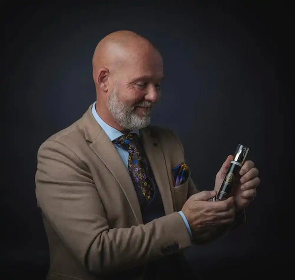 Mannelijke model toont met zorg een luxe gezichtsserum tegen veroudering in chique setting met donkere achtergrond.